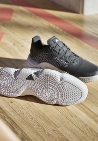 Black athletic shoes with a textured upper and lace closure, featuring a white, ridged sole with spiral patterns and an Adidas logo.