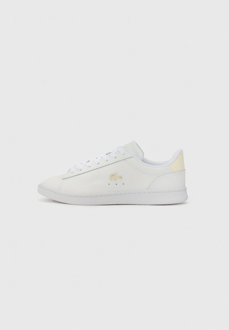 Hvit sneaker med glatt skinnoverside, rund tå, flate hvite snørebånd, gulllogo detalj på siden, og en beige detalj på hælen.