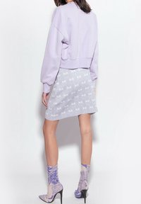 Laventelinvärinen lyhyt collegepaita yhdistettynä vaaleanharmaaseen minihameeseen, jossa on hillitty kuviointi. Malli käyttää kuvioituja nilkkasukkia ja korollisia kenkiä.