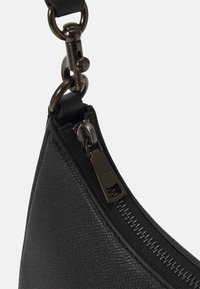 Gros plan d'un coin de sac en cuir noir texturé avec une fermeture éclair métallique et un fermoir reliant une sangle noire.