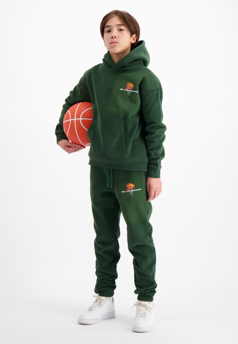Groene hoodie en bijpassende joggers met boordjes, voorzien van een basketbal grafiek en logo. De persoon houdt een oranje basketbal vast.