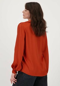 Roestkleurige blouse van gladde stof, met lange mouwen en geplooide manchetten, in een relaxte pasvorm.
