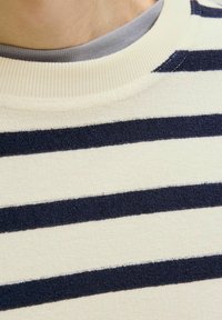 Jersey a rayas con franjas horizontales en crema y azul marino, cuello acanalado y tejido suave y texturizado. Vista en primer plano del diseño.