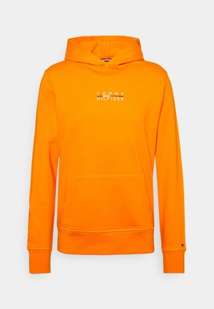 Orange cotton hoodie features a front pocket, ribbed cuffs, and a white logo text "TOMMY HILFIGER" on the chest. Smooth texture.