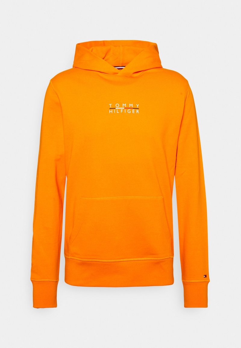 Pomarańczowa bawełniana bluza z kapturem ma przednią kieszeń, ściągacze na rękawach oraz biały napis "TOMMY HILFIGER" na klatce piersiowej. Gładka tekstura.