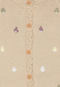 Bež pleteni kardigan s ruffled izrezom, drvenim dugmadima i izvezenim cvjetnim detaljima u zelenoj, ljubičastoj, žutoj i bijeloj boji.