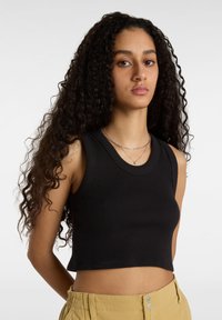 Svart ribbad crop top med vid halsringning och ärmlös design, med en figurnära passform och mjuk textur. Kombinerad med ljus khaki-byxor.