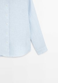 Chemise à manches longues bleu clair avec fines rayures blanches verticales, devant boutonné et poignets boutonnés, présentée sur un fond blanc.