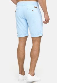 Shorts de algodón con dobladillo en azul claro, que cuentan con dos bolsillos traseros con botones de madera y una etiqueta de marca de cuero en la cinturilla.