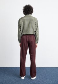 Striped green button-up shirt, brown elastic waistband pants, white shoes, viewed from the back, plain background, soft texture visible.
