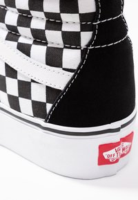 Hochschuh mit einem schwarz-weißen karierter Muster, aus Wildleder und Canvas-Materialien, weißen Nähten und einem roten Logotag an der Ferse.