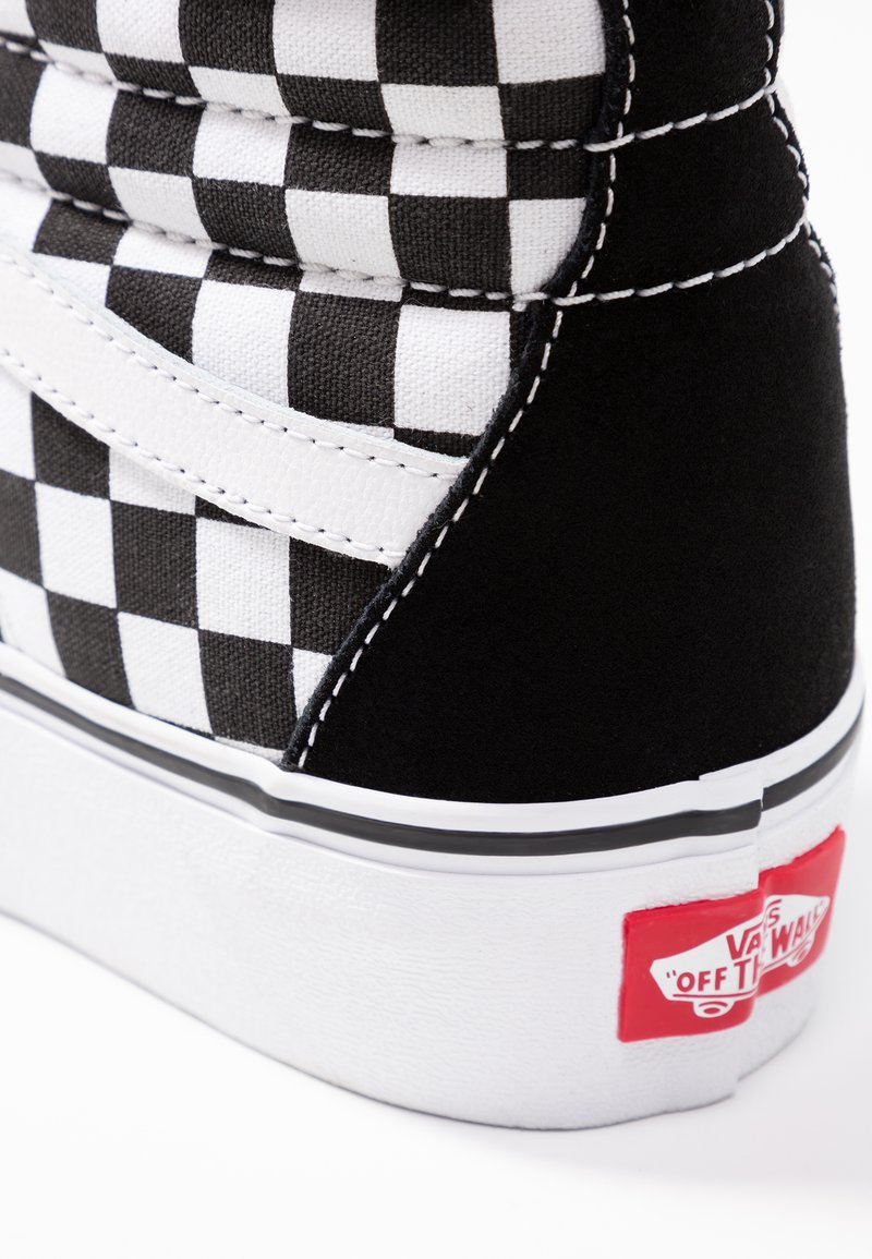 Basket montante avec un motif à carreaux noir et blanc, en suède et en toile, avec des coutures blanches et une étiquette rouge sur le talon.
