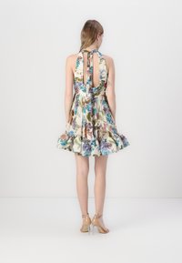 Robe florale avec un décolleté halter, un dos nu et une jupe évasée. Présente une base blanche avec des motifs floraux bleus, verts et violets.