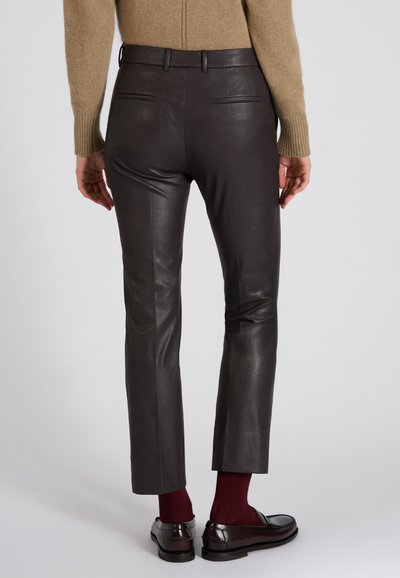 Ciemnobrązowe skórzane spodnie o dopasowanym kroju, z tylnymi kieszeniami i gładką teksturą, w połączeniu z bordowymi skarpetkami i czarnymi loafersami.