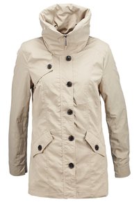 Chaqueta beige con un cuello alto, cierre de cremallera y seis botones negros en la parte delantera. Tiene dos bolsillos laterales con solapas en ángulo.