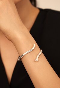 Bracelet en argent avec un design lisse et courbé ; présente une forme élancée et une extrémité arrondie. Fini propre, esthétique moderne.