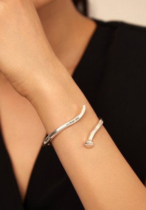 Bracelet en argent avec un design lisse et courbé ; présente une forme élancée et une extrémité arrondie. Fini propre, esthétique moderne.