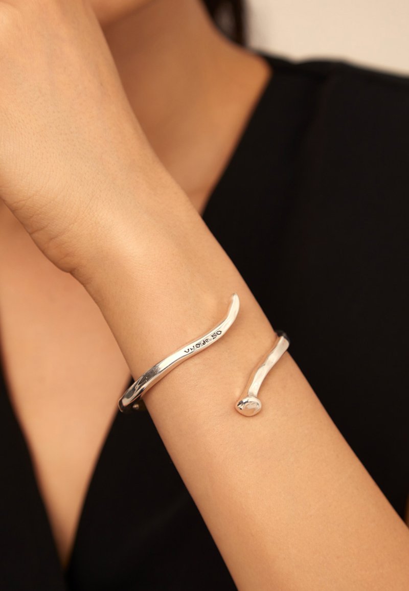 Bracelet en argent avec un design lisse et courbé ; présente une forme élancée et une extrémité arrondie. Fini propre, esthétique moderne.