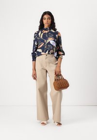 Blusa floreale navy con colletto arricciato, pantaloni beige a gamba larga e borsa in pelle marrone testurizzata. L'outfit presenta vari motivi botanici.