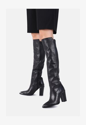 Botas de cuero negras hasta la rodilla con punta afilada y tacón ancho. Presentan un perfil delgado, una textura suave y un detalle de cremallera lateral.