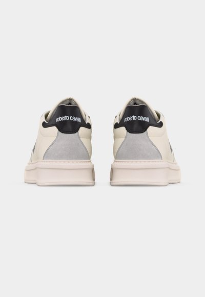 Ζεύγος λευκών και γκρι αθλητικών παπουτσιών με μαύρα τακούνια που φέρουν λευκή επωνυμία "roberto cavalli", εμφανιζόμενα από πίσω σε απλό φόντο.