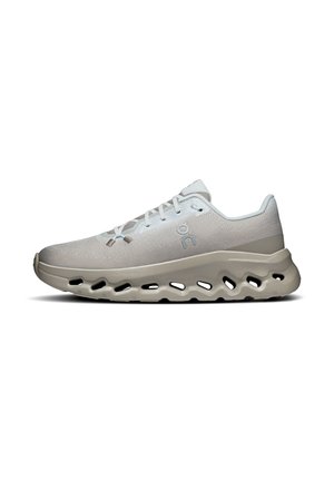 Chaussure de sport gris clair avec semelle épaisse comportant des découpes ovales, fermeture à lacets et logo subtil sur le côté, présentée de profil sur fond blanc.