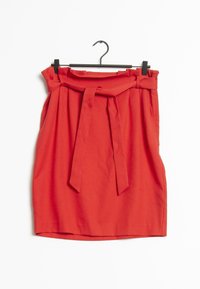 Rode hoge taille rok met plooien en een bijpassende stoffen riem geknoopt aan de voorkant, hangend aan een zwarte hanger tegen een witte achtergrond.