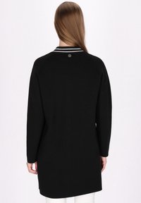 Schwarzer Langarm-Pullover mit rundem Kragen, versehen mit weißen Streifen. Glatte Textur mit einem kleinen Markenknopf auf der Rückseite.