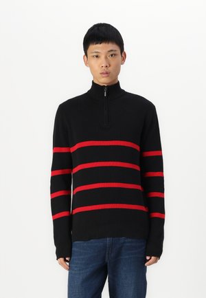 Black ribbed pullover sweater featuring red horizontal stripes, high collar with a zip closure, and long sleeves. Worn with blue jeans.