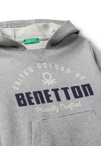 Sudadera con capucha gris con el texto "United Colors of Benetton", etiqueta verde y bolsillo delantero, mostrando una suave textura de tejido.