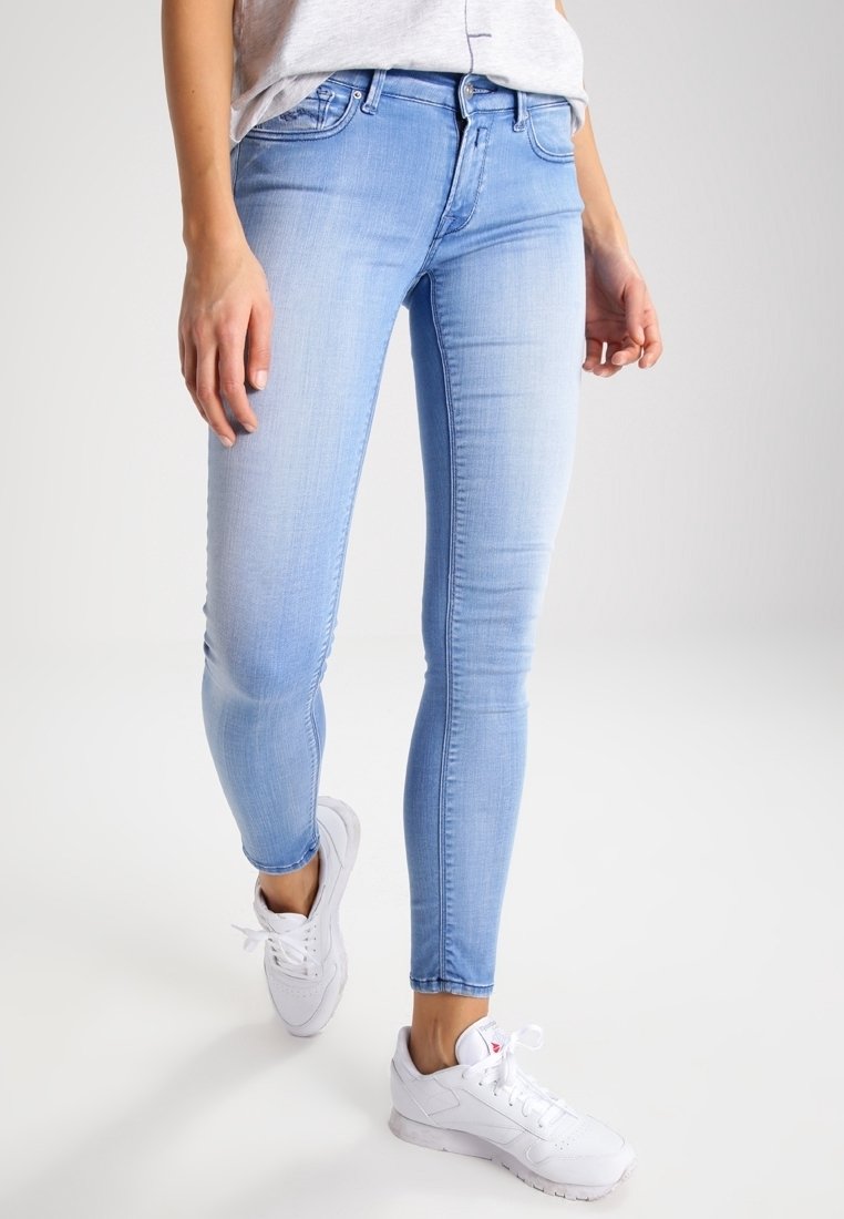 Jeans ajustados de mezclilla azul claro con un ligero efecto desgastado. Cuentan con un diseño de cinco bolsillos y se combinan con zapatillas deportivas blancas.