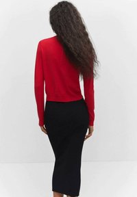 Haut rouge à manches longues associé à une jupe midi noire côtelée. Le haut présente une coupe ajustée, et la jupe a une texture lisse.