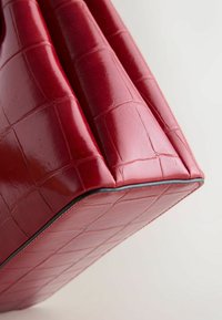 Rote Kunstleder-Handtasche mit gestepptem Muster, eckiger Form und glatter Oberfläche. Schwarze Kanten betonen die unteren Nähte.