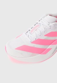 Biały i różowy but do biegania Adidas Adizero z sznurówkami i widoczną amortyzacją Lightstrike Pro na podeszwie na białym tle.