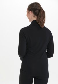 Langærmet sort træningsskjorte med høj krave, flade sømme og tætsiddende design. Glat stofstruktur; strømlinet, minimalistisk æstetik.