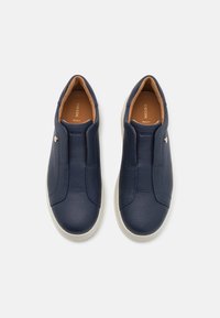 Paire de baskets bleu marine sans lacets avec semelles blanches et doublure intérieure couleur beige, vue de dessus sur fond blanc.