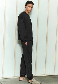 Zwart sweatshirt en jogger set, gemaakt van zachte stof. Het sweatshirt heeft een ronde hals en drop schouders; de joggers hebben zijzakken en elastische manchetten.