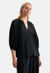 Blusa nera leggera con scollatura a V e dettagli arricciati alle spalle. Presenta maniche lunghe tre quarti ampie. Texture liscia.