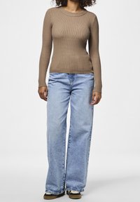 Haut marron à manches longues côtelées avec un col rond, associé à un jean large bleu clair. Le tissu semble doux avec une finition texturée.