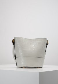 Borsa a secchiello grigia con motivo coccodrillo, texture liscia, tracolla nera e dettagli in metallo dorato. Presenta una parte superiore arrotondata e una base piatta.