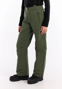Groene waterdichte sneeuwbroek met verstelbare banden, zijrits zakken en een rechte broekspijp. Gemaakt in combinatie met zwarte, textuur-schoenen.