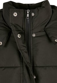 Black padded jacket with a high collar, featuring a front zipper and snap buttons, made from smooth, weather-resistant fabric.