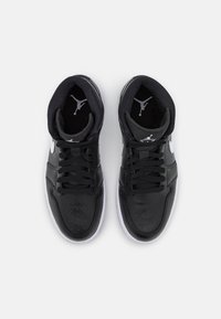 Schwarze Leder-Sneaker mit einem hohen Design, durchbrochener Zehenbox, weißer Sohle und kontrastierenden Logo-Akzenten auf der Zunge und den Seiten.