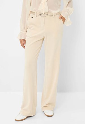 Pantalons en velours côtelé beige dotés d'une taille cintrée avec une ceinture, de jambes larges et d'une surface texturée. Associés à des chaussures blanches pour le contraste.