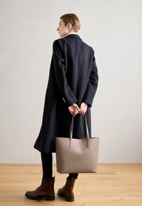 Hnědé kožené boty, tmavý kabát a béžová taška s dlouhými uchy. Jednoduchý design a hladká textura, umístěné na světlém pozadí.