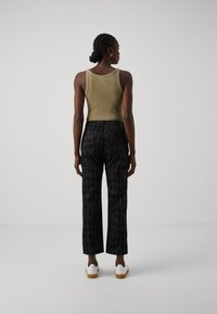 Olivgrünes, geripptes Tanktop, kombiniert mit schwarzen, bedruckten, weiten Hosen und weißen Schuhen. Die Hose hat ein dezentes Design und eine glatte Textur.