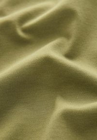 Tissu vert olive doux avec une texture fine en maille et des plis délicats créant des ombres subtiles et des reflets.