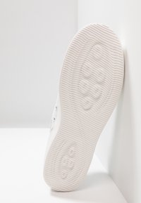 Den vita sneakersulan har ett strukturerat, ribbat mönster för grepp, med en platt, rundad form och minimal detaljering på ytan.