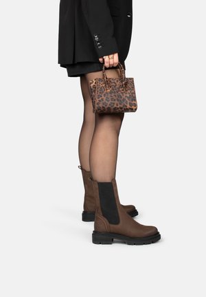 Bottines en daim marron avec des panneaux élastiques noirs, semelles épaisses, assorties à un petit sac à main en imprimé léopard. Un blazer noir et un short sont visibles.