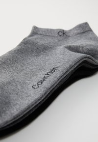 Calzini grigi realizzati in tessuto a maglia fine, con un logo nero "Calvin Klein" vicino al gambale, caratterizzati da una texture liscia e senza motivi visibili.